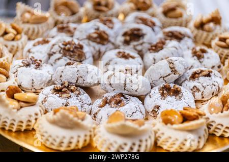 Photo horizontale une sélection vibrante de pâtisseries arabes aux noix, saupoudrées de sucre en poudre et présentées sur un plateau doré orné, prêtes pour une fête Banque D'Images