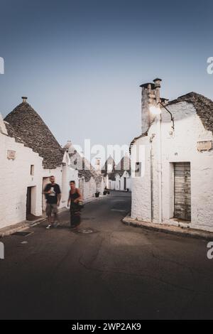 ITALIE, POUILLES, ALBEROBELLO : vue sur la rue des trulli d'Alberobello au coucher du soleil. La ville d'Alberobello est connue comme la capitale des trulli, les bâtiments en pierre caractéristiques avec un toit conique qui jamais comme les autres, représentent dans l'imagination, toute la région des Pouilles. Il est né comme un bâtiment de base pour les besoins agricoles, les trulli étaient en fait utilisés comme abris temporaires, dépôts, écuries, et comme la technique a été affinée, comme maisons. Banque D'Images