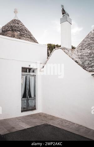 ITALIE, POUILLES, ALBEROBELLO : vue sur la rue des trulli d'Alberobello au coucher du soleil. La ville d'Alberobello est connue comme la capitale des trulli, les bâtiments en pierre caractéristiques avec un toit conique qui jamais comme les autres, représentent dans l'imagination, toute la région des Pouilles. Il est né comme un bâtiment de base pour les besoins agricoles, les trulli étaient en fait utilisés comme abris temporaires, dépôts, écuries, et comme la technique a été affinée, comme maisons. Banque D'Images