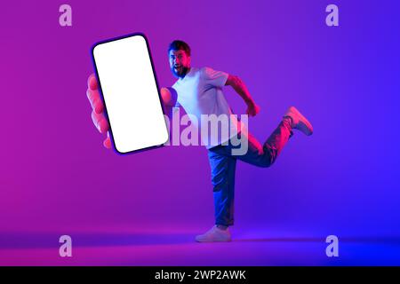 Excité Guy montre énorme smartphone avec écran vierge, fond de néon Banque D'Images