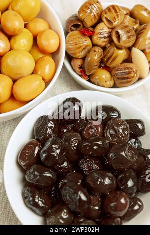 un ensemble de trois types d'olives dans des bols blancs - grandes olives vertes entières, olives noires, olives vertes grillées à l'huile, dénoyautées, vue de dessus, gros plan, fragm Banque D'Images