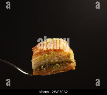 un délicieux baklava au miel avec des pistaches sur une fourchette sur un fond noir, vue de côté Banque D'Images