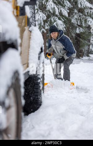 Un homme est en train de déneiger la route. La neige est entassée sur le sol et l'homme utilise une pelle pour la nettoyer Banque D'Images