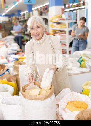 Femme âgée remplissant le sac en plastique avec de la farine de maïs dans le magasin d'alimentation Banque D'Images