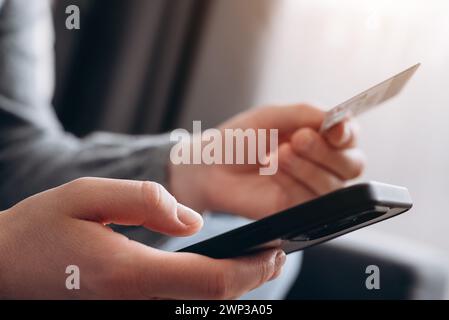 Gros plan des mains féminines tenant une carte de crédit et un smartphone, femme inconnue payant en ligne, en utilisant le service bancaire, en saisissant des informations, des achats, une commande Banque D'Images