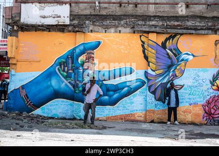 Deux hommes se tiennent devant des peintures murales représentant une main tenant une ville et un oiseau volant peint sur un mur dans la ville de Nakuru, créé dans le cadre du projet de ville créative de l'UNESCO de Nakuru pour mettre en valeur le patrimoine culturel et artistique de la ville. Ce travail collaboratif met en vedette les contributions de divers artistes de graffiti dont Bankslave, Joel Bergner, Chelwek, Dante et Natasha Floortje. Banque D'Images