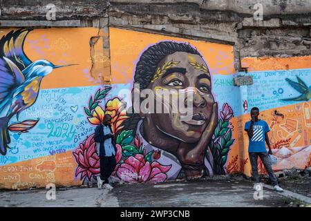 Deux hommes se tiennent debout à côté d'une murale représentant une femme africaine peinte sur un mur dans la ville de Nakuru, créée dans le cadre du projet de ville créative de l'UNESCO de Nakuru pour mettre en valeur le patrimoine culturel et artistique de la ville. Ce travail collaboratif met en vedette les contributions de divers artistes de graffiti dont Bankslave, Joel Bergner, Chelwek, Dante et Natasha Floortje. Banque D'Images