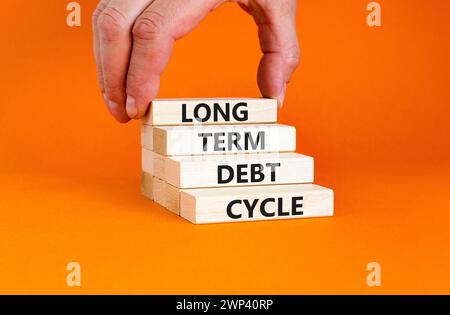 Symbole du cycle de la dette à long terme. Mots conceptuels cycle de dette à long terme sur beau bloc de bois. Belle table orange fond orange. Main d'homme d'affaires. Banque D'Images