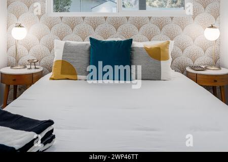 Chambre moderne avec lit confortable, oreillers, tables de nuit et papier peint en mosaïque Banque D'Images