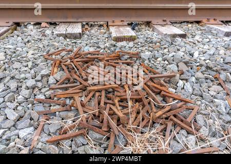 Pile de pointes rouillées de chemin de fer sur pierre concassée à côté des voies ferrées. Banque D'Images