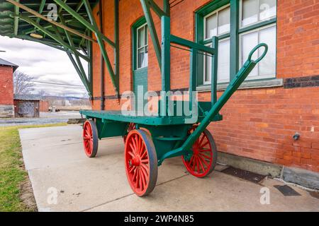 Chariot à bagages en bois vert vintage avec quatre roues de wagon le long d'un bâtiment en briques. Banque D'Images