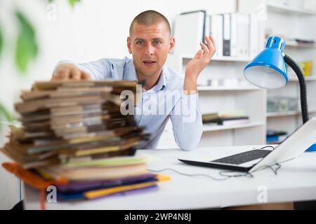 Homme d'affaires choqué assis à la table de bureau avec de nombreuses chemises de papier Banque D'Images