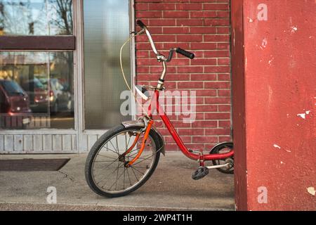 Vieux vélo rouge appuyé sur un poteau en béton devant le bâtiment résidentiel, mise au point sélective Banque D'Images