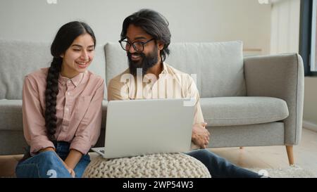 Couple multiracial homme arabe et femme indienne sur le plancher famille couple propriétaires femme petite amie et mari petit ami regardant le film portable Smart TV Banque D'Images