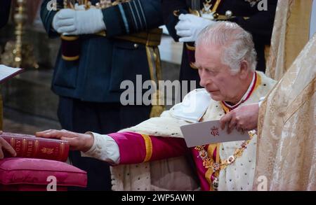 Le roi Charles III couronnement, assis dans des robes de cérémonie, prête le serment solennel couronnement touchant la Sainte Bible gravée avec ses souverains Cypher et date, lors de la cérémonie de service du couronnement à l'abbaye de Westminster Westminster Londres Royaume-Uni le 6 mai 2023 Banque D'Images