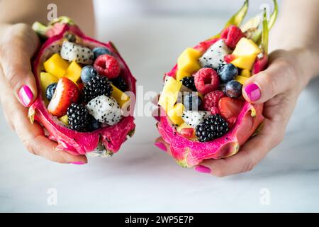 Mains tenant des coquilles de fruits de dragon remplies de salade de fruits frais. Banque D'Images