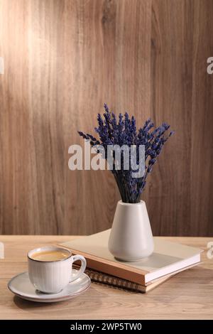 Bouquet de belles fleurs de lavande conservées, cahiers et tasse de café sur table en bois à l'intérieur Banque D'Images