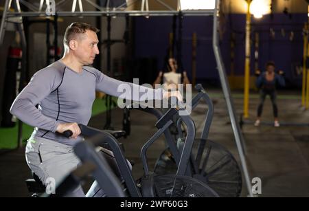 Homme actif faisant de l'entraînement cardio sur vélo stationnaire cross training dans le gymnase Banque D'Images
