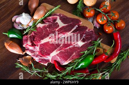 Morceaux de steaks de viande de bœuf frais sur un bureau en bois avec légumes et romarin Banque D'Images