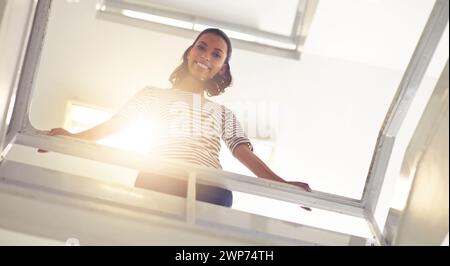Angle bas, femme d'affaires et portrait pour la confiance par les escaliers, bureau et professionnel par balustrade. Personne féminine, heureuse et fierté d'entrepreneur pour Banque D'Images