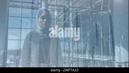Image de graphiques financiers sur une femme d'affaires biraciale dans le hijab marchant dans le bureau Banque D'Images