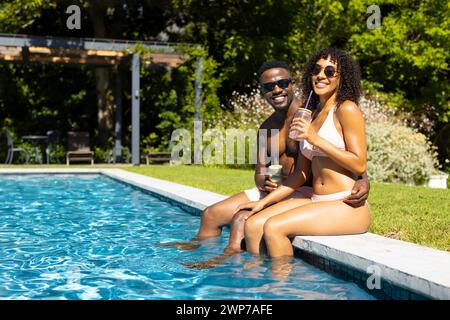 Un couple biracial profite d'une journée ensoleillée au bord de la piscine avec espace de copie Banque D'Images