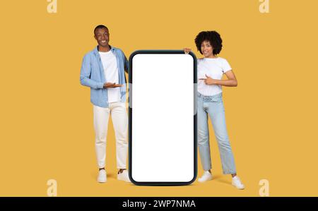 Couple afro-américain engageant présentant un grand écran de smartphone blanc vertical Banque D'Images