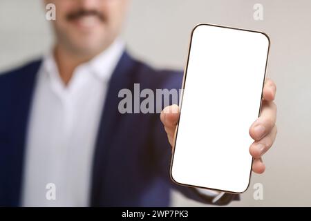 Homme d'affaires flou dans une veste bleue et chemise blanche présentant un smartphone avec un écran vierge Banque D'Images
