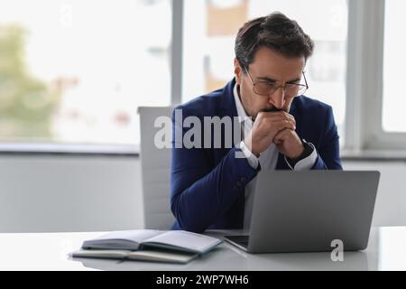 Homme d'affaires pensif en costume bleu profondément concentré sur son écran d'ordinateur portable Banque D'Images