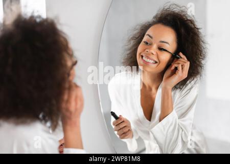 femme noire applique le mascara sur les cils pendant la routine dans la salle de bain Banque D'Images