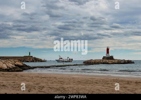 Villajoyosa, Espagne, 04 mars 2024:paysage maritime avec bateau de pêche entrant dans le port de Villajoyosa à côté du phare et ciel nuageux au Banque D'Images