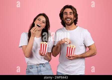 Femme et homme joyeux en t-shirts blancs riant et mangeant du pop-corn dans des boîtes rayées rouges et blanches Banque D'Images