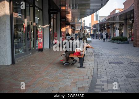 Novara, Italie, 16 janvier 2024 : femme assise sur un banc abreuvant un chien au centre commercial Vicolungo The style Outlets Banque D'Images