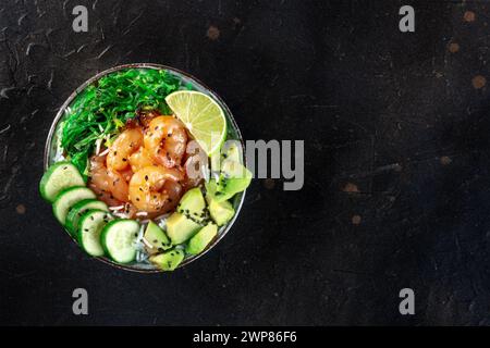 Bol de poke de crevettes avec avocat, concombres, wakame et citron vert, tourné d'en haut sur un fond noir avec une place pour le texte Banque D'Images