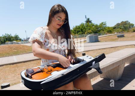 Femme de busker Latina assise dans la rue mettant du violon dans son cas après avoir fait de l'art et joué du violon. Banque D'Images
