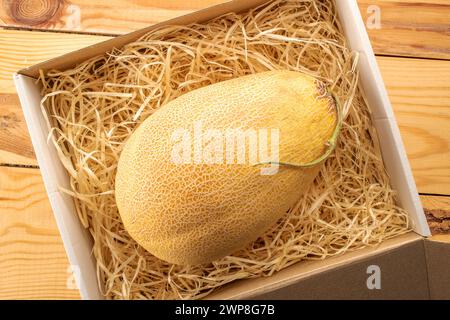 Un melon doux mûr dans une boîte de papier avec des copeaux de bois sur une table en bois, macro, vue de dessus. Banque D'Images