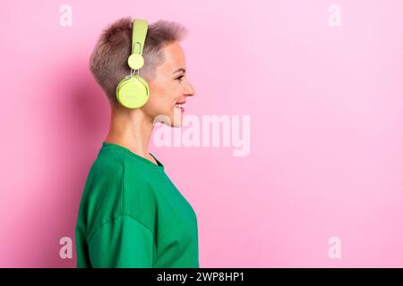 Photo de profil de belle femme joyeuse sourire dentelé écouter de la musique écouteurs espace vide isolé sur fond de couleur rose Banque D'Images