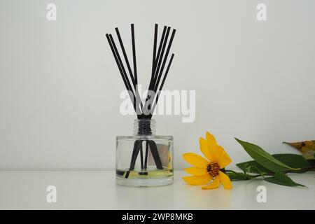 Bâtonnets d'arôme dans un vase cubique en verre avec des huiles essentielles. Décoration intérieure. Fond blanc. Fleur d'artichaut de Jérusalem jaune sur la table. Natures mortes c Banque D'Images