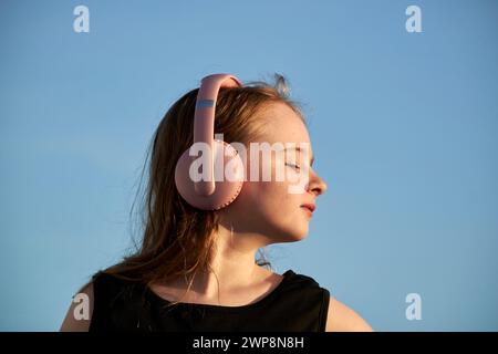 Jeune fille irlandaise britannique de 10 ans portant une robe noire et des écouteurs pendant l'heure d'or coucher du soleil Lanzarote, îles Canaries, espagne Banque D'Images