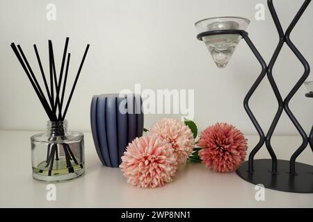 Composition avec des bâtonnets d'encens, de l'huile essentielle dans un vase en verre et des fleurs artificielles éponge rose. Grand lustre en métal avec supports en verre pour les petits Banque D'Images