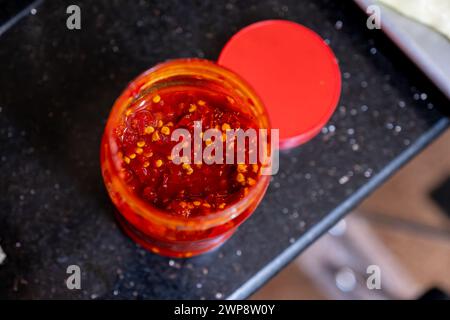Sauce traditionnelle adjika au piment fort, collez l'harissa dans un pot en verre sur une table brune Banque D'Images