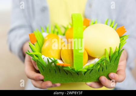 3 mars 2024 : petit garçon tenant un nid de Pâques en feutre rempli d'oeufs de Pâques à Pâques *** Kleiner Junge hält ein Filz Osternest gefüllt mit Ostereiern an Ostern in der Hand Banque D'Images