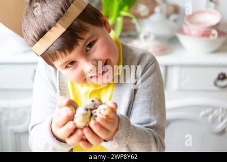 3 mars 2024 : chasse aux œufs, petit garçon tenant plusieurs œufs de caille pour Pâques. Enfant avec des oreilles de lapin faites soi-même sur la tête *** Eiersuche, Kleiner Junge hält mehrere Wachteleier zu Ostern in der hand. Kind mit selbstgebastelten Hasenohren auf dem Kopf Banque D'Images