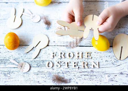 3 mars 2024 : joyeuses Pâques, salutation écrite avec des lettres en bois à côté des mains des enfants faisant des décorations de Pâques *** Frohe Ostern, Gruß geschrieben mit Holzbuchstaben neben Kinderhänden die Osterdekoration basteln Banque D'Images