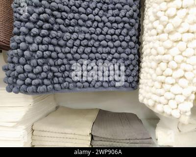 Les tapis de bain en microfibre blanc et gris sont suspendus au comptoir du magasin. Style scandinave. Tapis rectangulaires en tissu doux avec boutons tricotés. D Banque D'Images