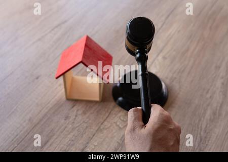 Main tenant le marteau à côté de la maison miniature en bois. Vente aux enchères de maisons, expropriation et concept d'expulsion. Banque D'Images