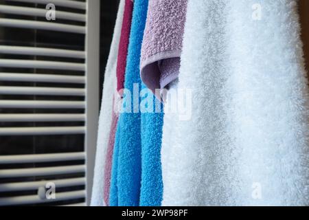 Les serviettes sont suspendues à côté d'un porte-serviettes chauffant, d'un radiateur mural ou d'un radiateur. Serviettes blanches, bleues, roses, rouges. Organisation des articles ménagers dans la salle de bain Banque D'Images