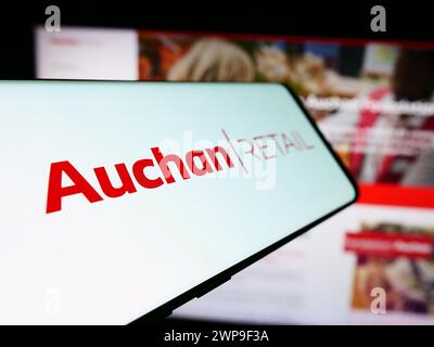 Smartphone avec logo de la société française Auchan Retail International sa devant le site Web de l'entreprise. Focus à gauche de l'écran du téléphone. Banque D'Images