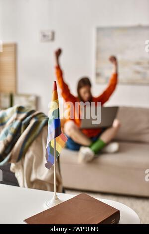 Concentrez-vous sur le drapeau LGBTQ sur le bureau près d'une adolescente floue assise les mains levées et un ordinateur portable Banque D'Images