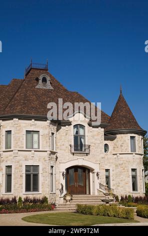 Vue partielle de la luxueuse maison en pierre taillée beige et beige de deux étages avec cour avant paysagée en été. Banque D'Images